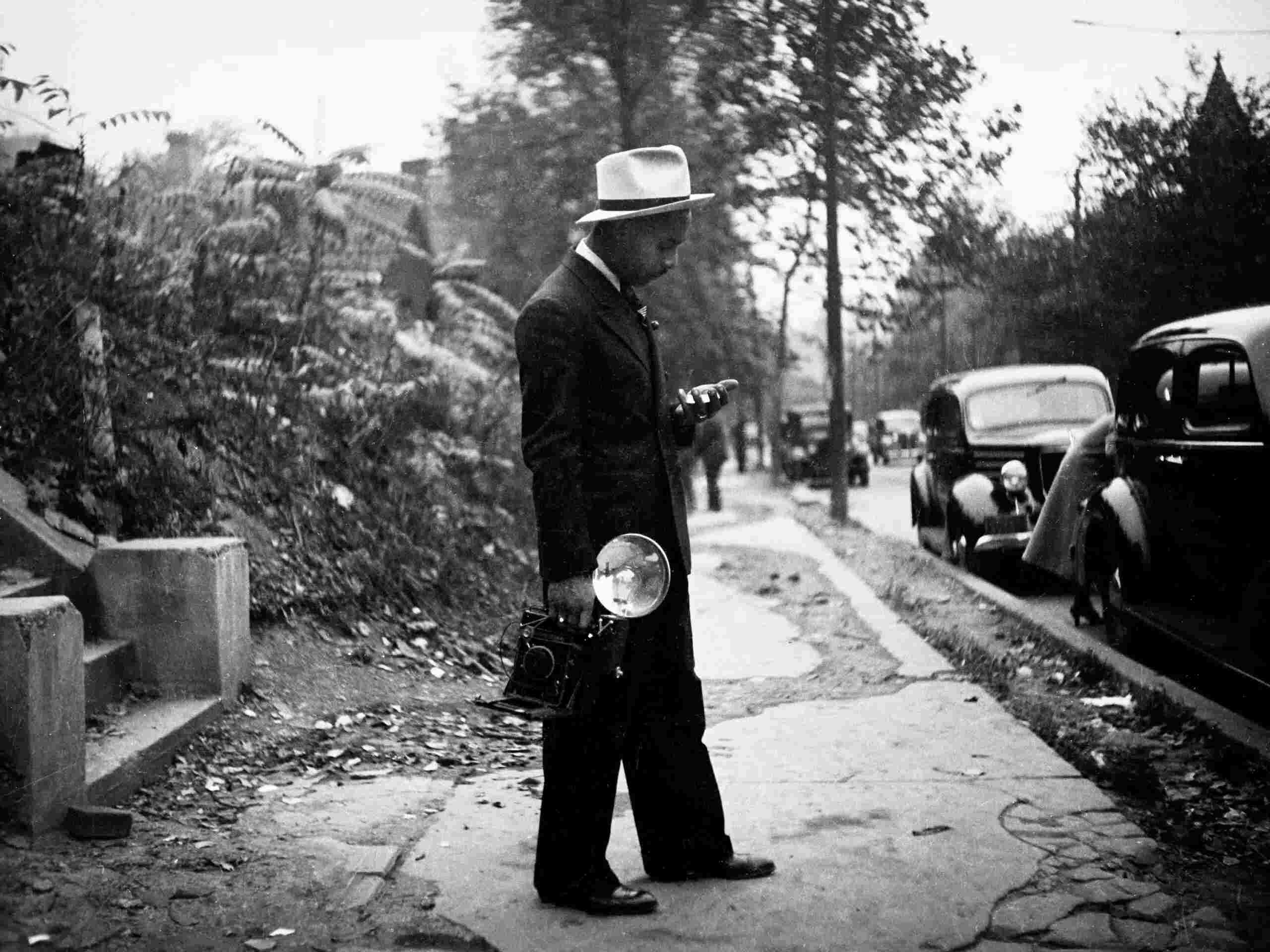 Photographer Charles “Teenie” Harris stands on a sidewalk holding his camera in Pittsburgh, ca 1938.